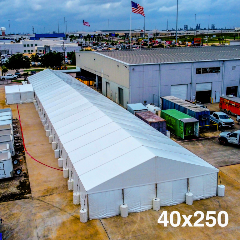 Aerial view of a long white structure tent set on pavement beside industrial warehouses