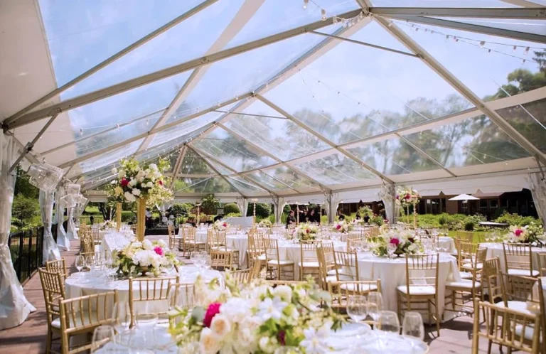 Clear top frame tent over round banquet tables with gold Chiavari chairs and floral centerpieces