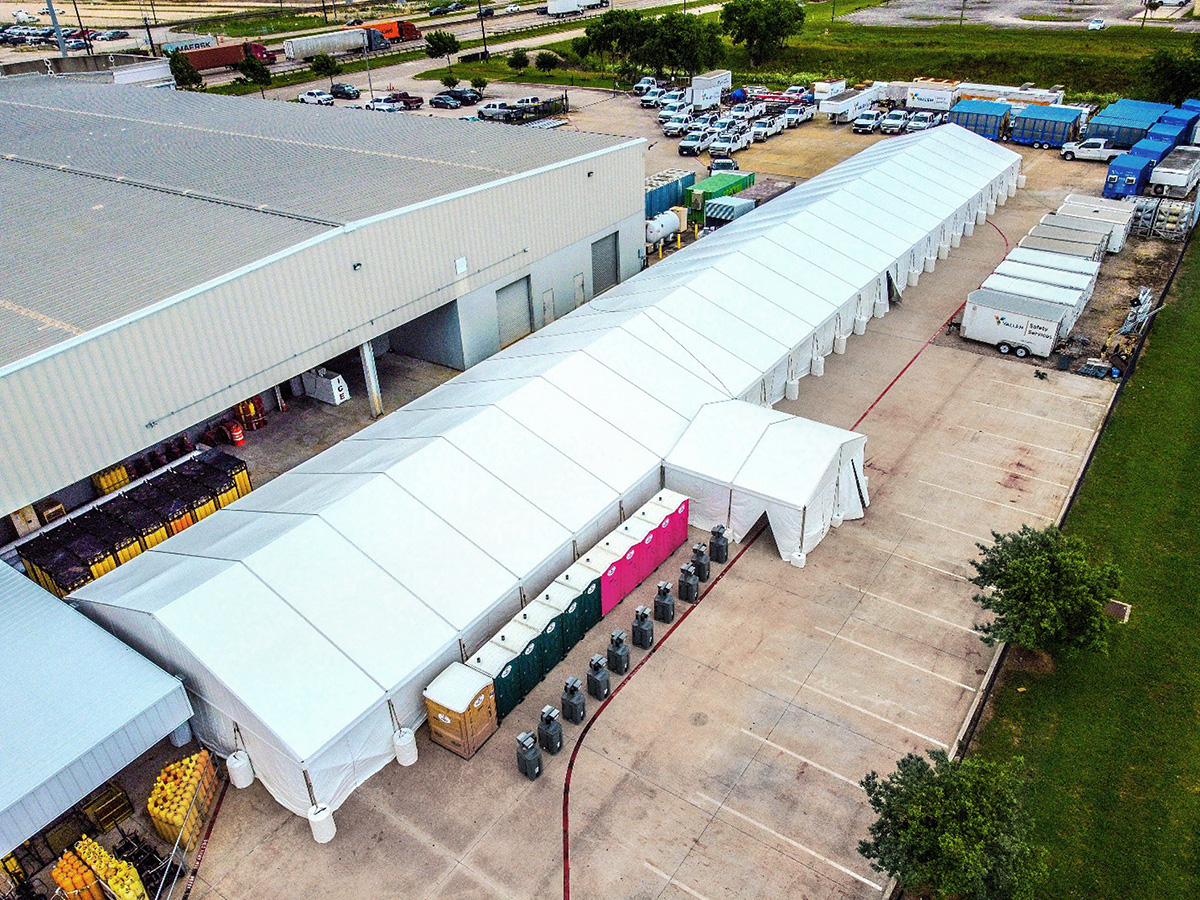Aerial view of a long white structure tent set up alongside a warehouse at an industrial site