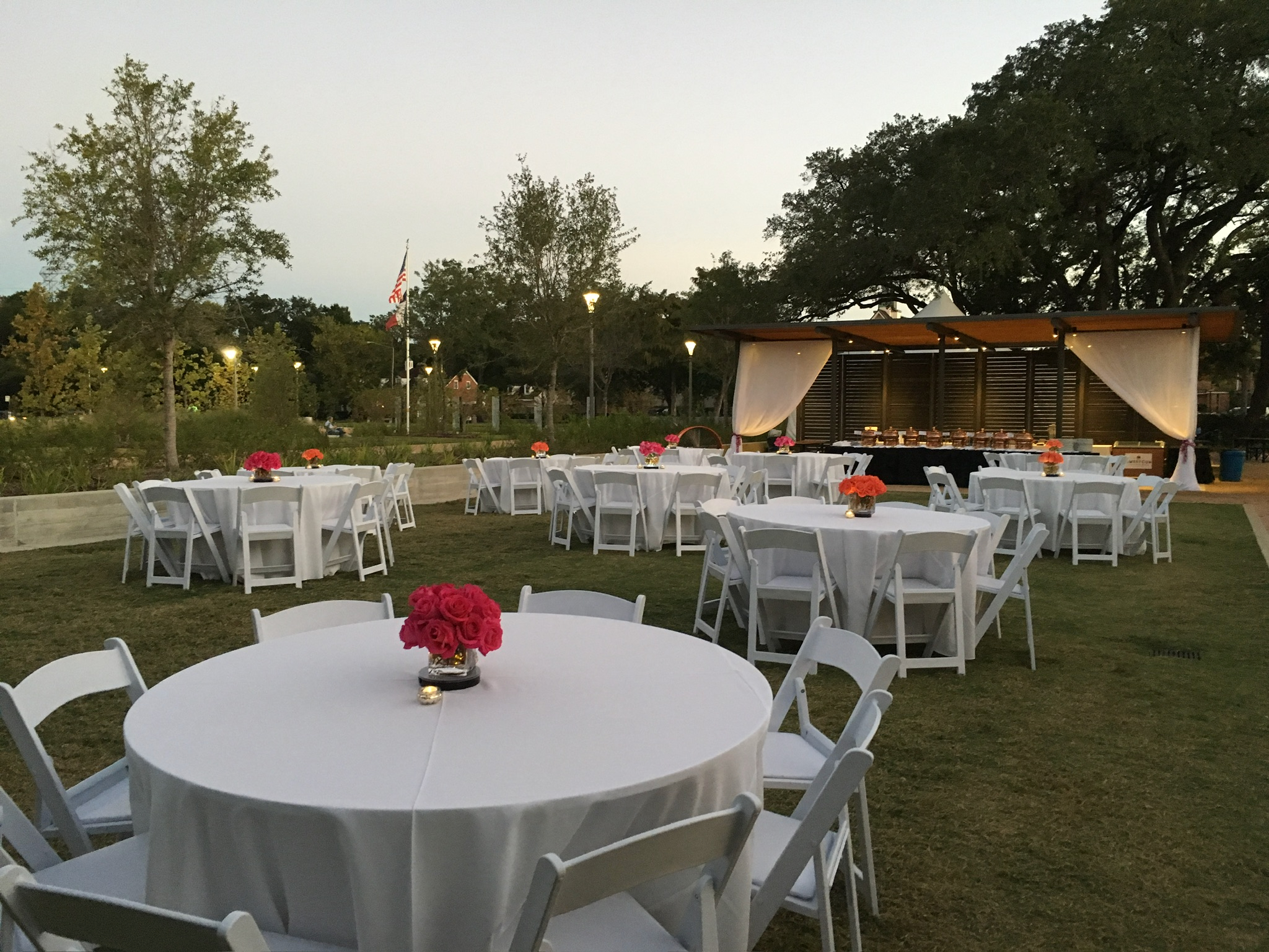White folding chairs at round tables on a Houston lawn at dusk, set for an outdoor event