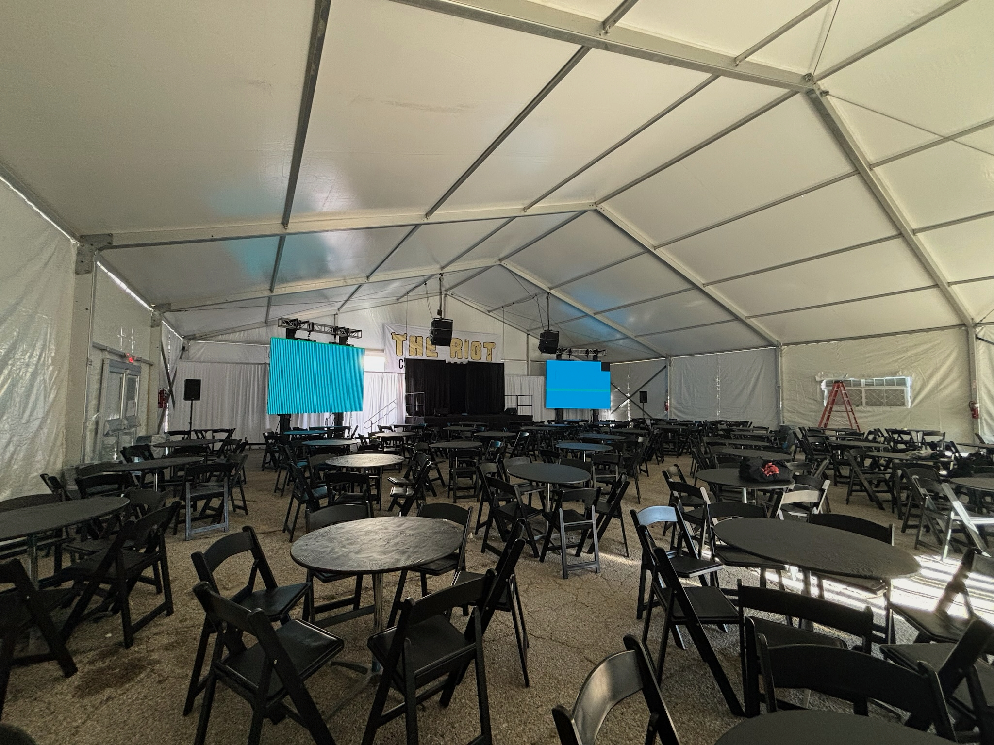 Black folding chairs and round tables laid out inside an ACME clearspan tent