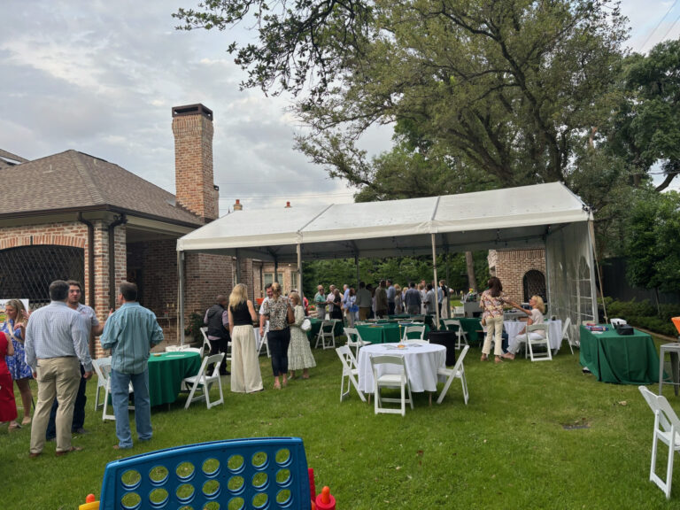 Guests mingling under a backyard frame tent with green linens at a Houston party
