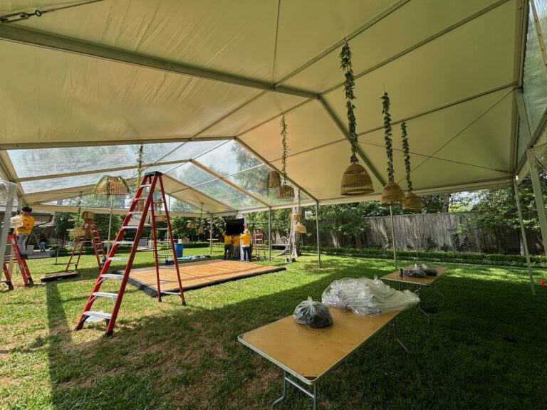 Crew on ladders hanging woven pendant lights in a clear top frame tent over a backyard dance floor